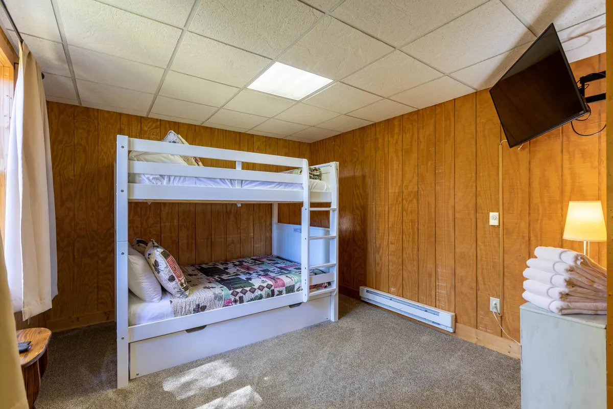 A bunk room featuring sturdy bunk beds, a TV, a lamp, and neatly folded towels. The space is playful yet cozy, designed to accommodate children or teens with entertainment options close at hand.