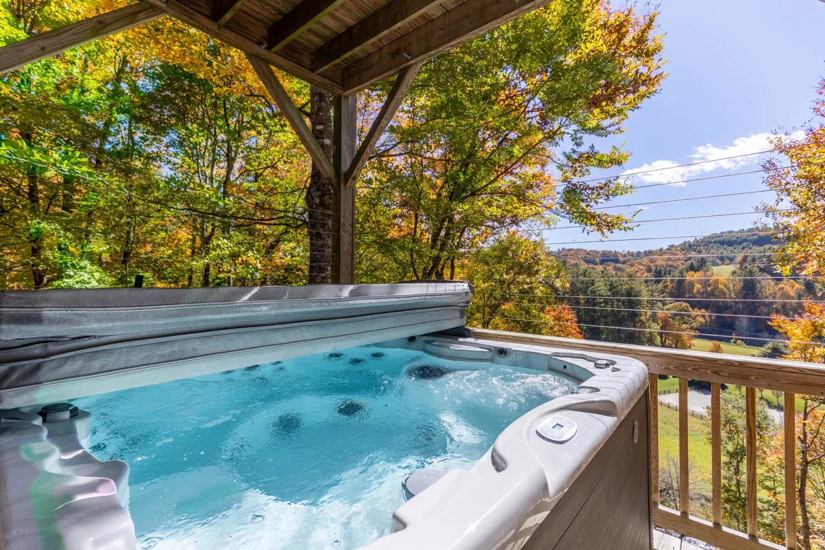 An exterior shot featuring a private hot tub on a deck surrounded by trees and mountains in the background. The inviting hot tub promises relaxation after a day of outdoor exploration, creating an ideal mountain retreat atmosphere.