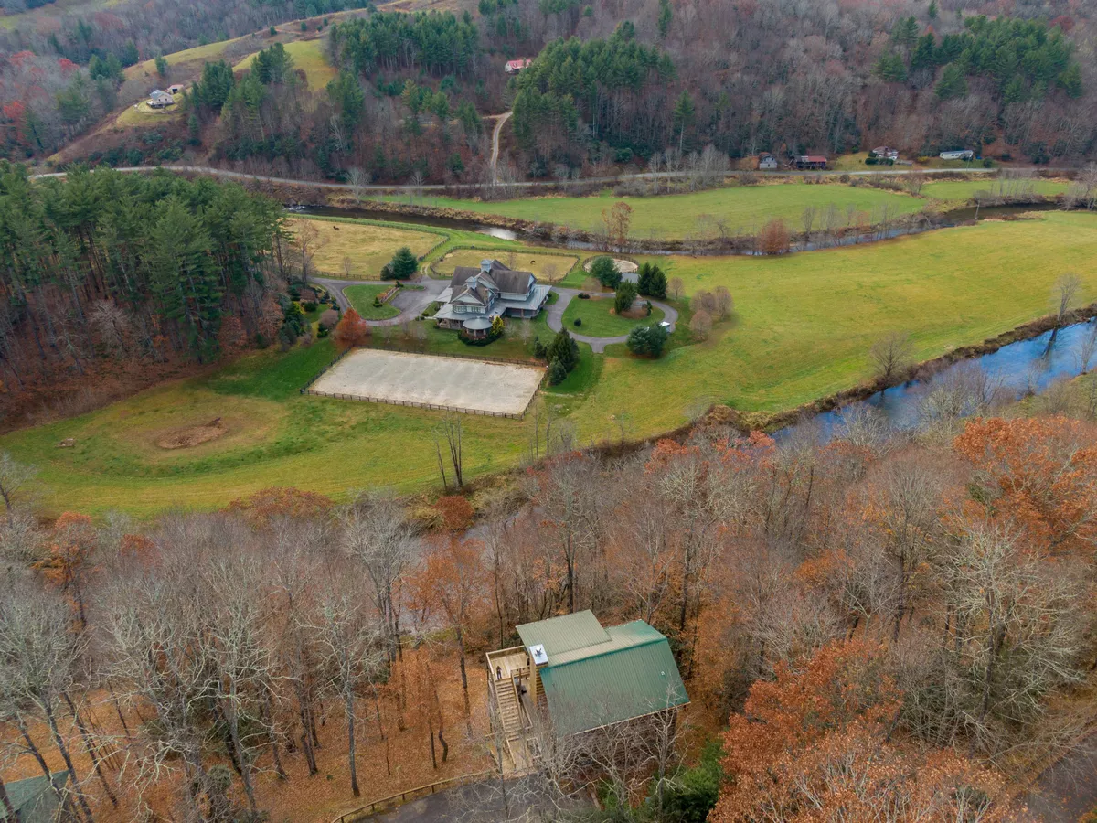 A wide view of the property reveals a large house surrounded by green fields, a winding river, and trees. The natural landscape surrounding the house suggests ample outdoor space for group activities, nature walks, and memorable family moments beyond the cabin walls.