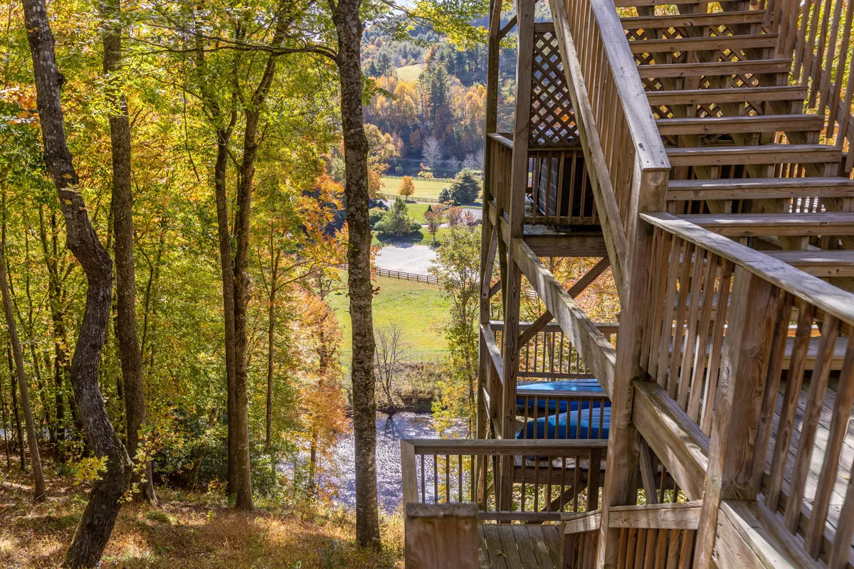 A wooden staircase descends through a vibrant forest of autumn foliage, leading the eye toward a serene river below. The view suggests opportunities for hiking, nature walks, and riverside exploration.