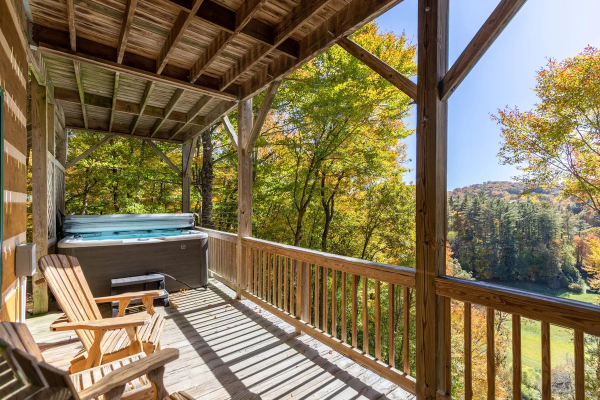 This photo captures the serene hot tub area set on a wooden deck, surrounded by lush trees and offering a panoramic mountain view. The inviting hot tub looks out onto nature, illustrating the promise of relaxation and scenic immersion.