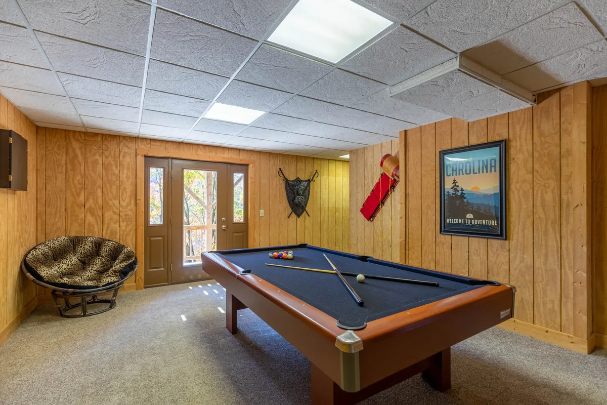 Here, the focus is on another angle of an interior pool table room, featuring double doors that likely open to the deck, a distinctive leopard-print chair, and framed wall art. The setting feels lively and welcoming for group activities, with easy access to both indoor fun and outdoor leisure.