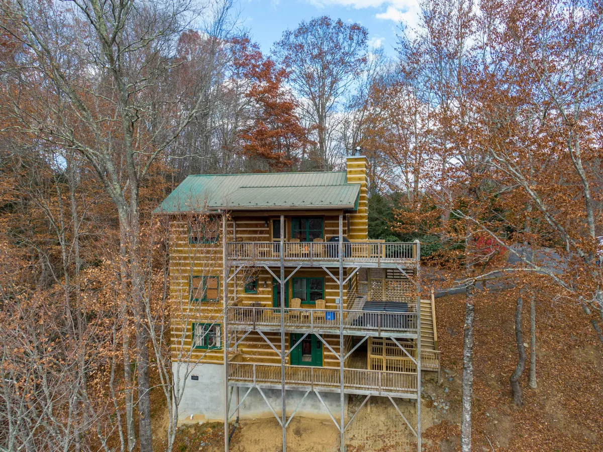 This image features the log cabin's exterior, highlighting its welcoming structure with large balconies and the surrounding trees. The scene conveys a sense of arrival and the inviting nature of the cabin, subtly suggesting areas where family and friends can gather outdoors.